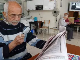 Gazeteleri büyüteçle okuyor
